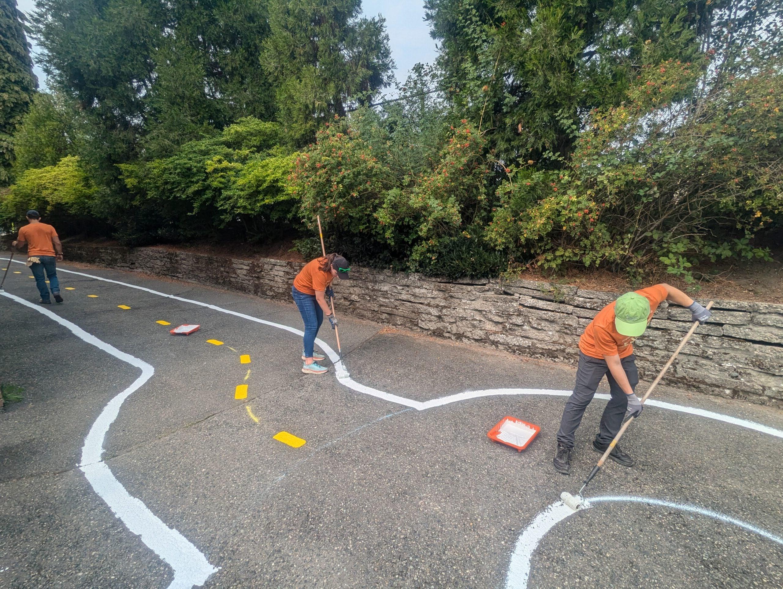 Three volunteers paint traffic garden street lines on pavement.