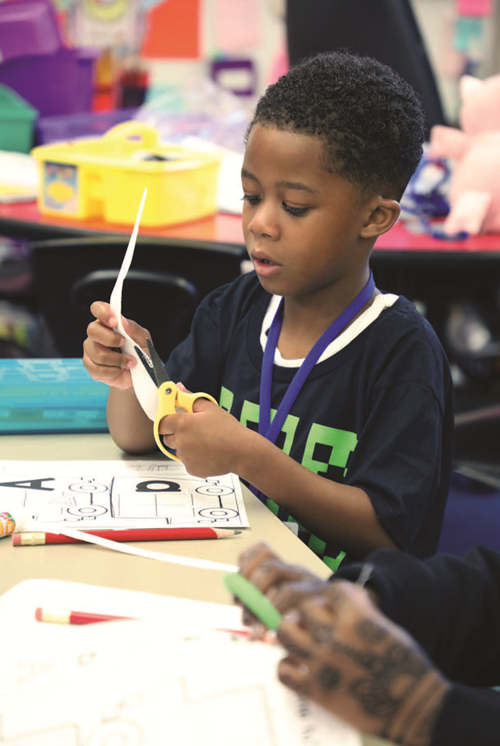 Preschool student cutting a piece of paper with scissors